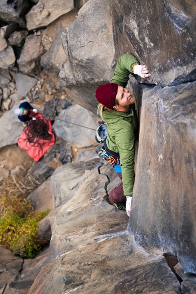 man in green jacket climbing on brown rock during daytime